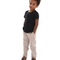 A boy with curly hair looking at the camera. He is wearing clothing from Moustache Kids. A black t-shirt, beige pants and coffee brown moccasin dress shoes. 