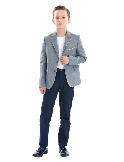 A young boy wearing a light blue gray blazer from Moustache Kids. He’s sporting a casual look with a white t-shirt, blue trousers and shiny black dress shoes. All from Moustache Kids. 