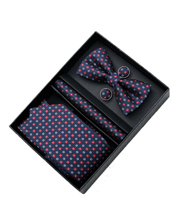 A multi colored red, white and blue bowtie, necktie, pocket square and cufflinks set from Moustache Kids. The white designs are circles, the red designs are small flowers and the backdrop of the textured clothing is navy blue. 