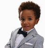 A young boy with curly hair playfully looking at the camera and smiling. He is wearing a Moustache Kids blue plaid blazer with a white dress shirt and pocket square. 