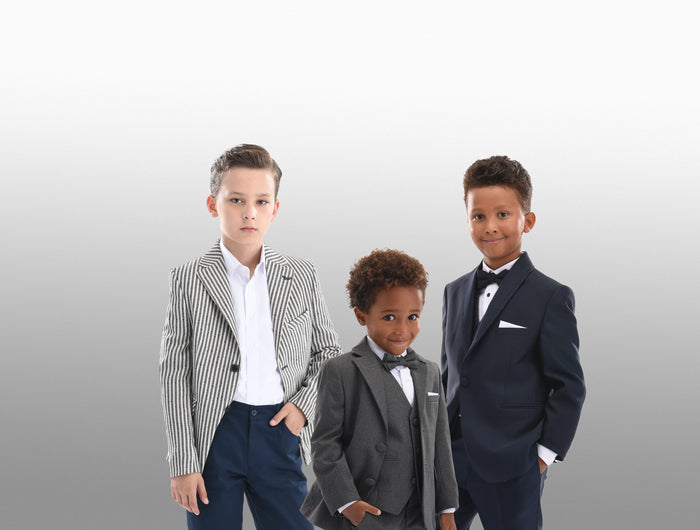 3 boys wearing Moustache Kids clothing. One is wearing a Moustache Kids Blazer, with white dress shirt and blue trousers. One is a gray 5 piece Tuxedo suit and the other is wearing a damascus blue 5 piece tuxedo suit